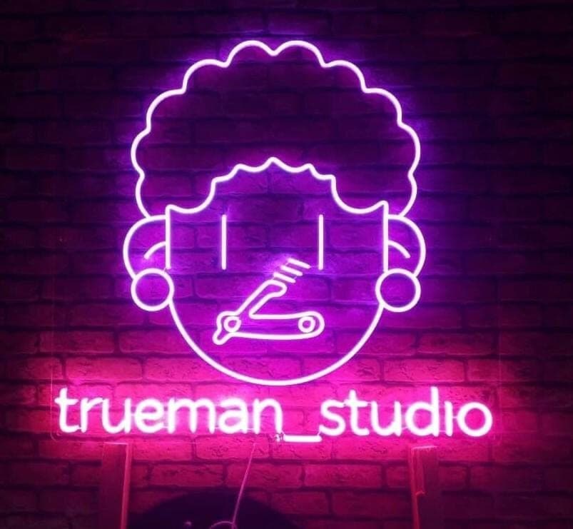 Неоновая вывеска True Man Studio на кирпичной стене